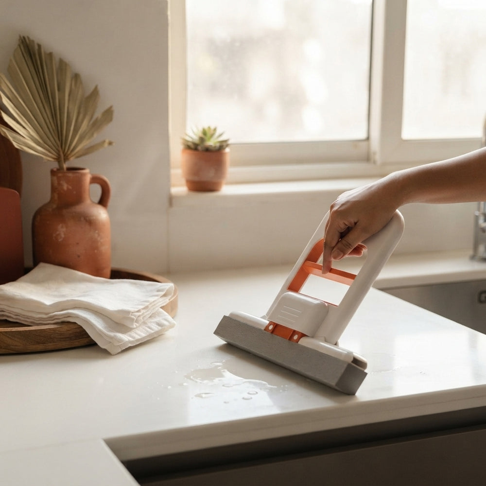 A person using a portable mini sponge mop to clean a small spill on a kitchen countertop in a home setting.
